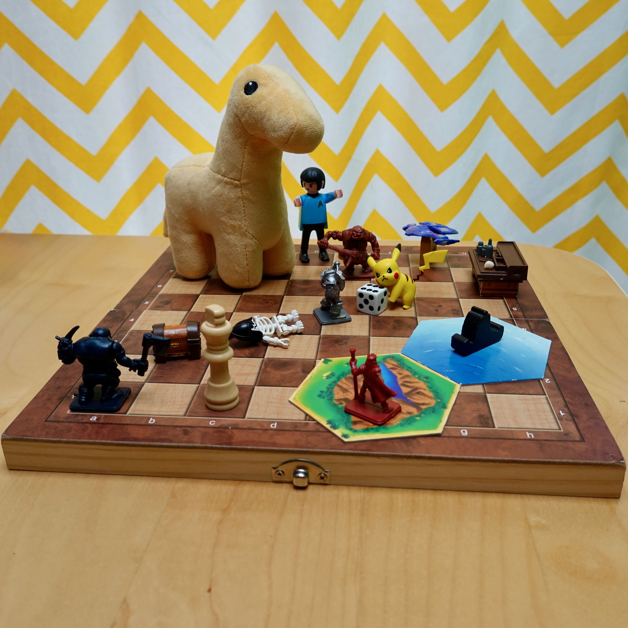 A plush brontosaurus standing on a chessboard surrounded by playing pieces from many different games